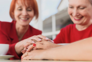 imagen de dos dos mujeres sonriendo y poniendo sus manos, una encima de otra, en una mesa 