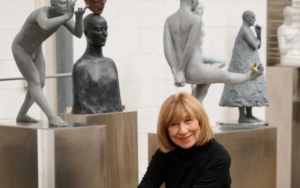 Imagen de Aurora Cañero mirando de frente sonriente sentada en un museo rodeada de sus esculturas