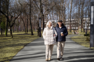 Pareja de personas abrigados un día de sol de paseo por un parque cogidos del brazo