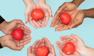 Imagen de varias manos haciendo círculo sosteniendo cada una un corazón rojo