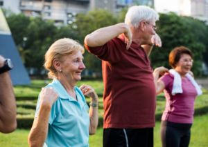 Imagen de dos personas mayores, dos mujeres y un hombre, con las manos en los hombros haciendo deporte en un parque 