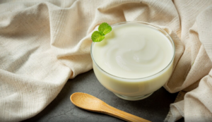 Imagen de un yogur natural en un recipiente de cristal con una cuchara de madera al lado