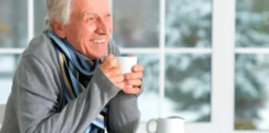 Hombre mayor con frio sosteniendo una taza de cafe caliente