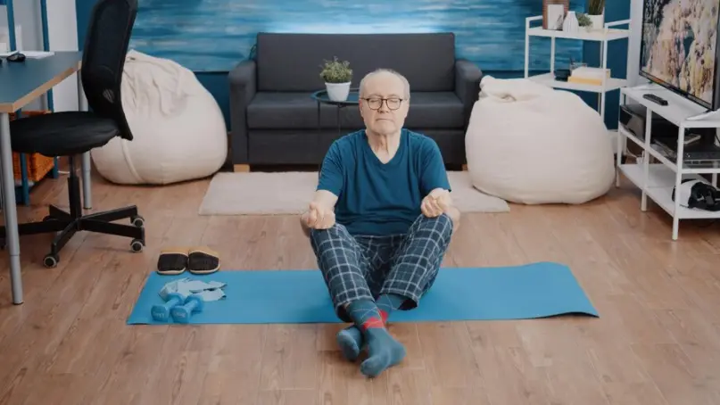 Hombre mayor con ojos cerrados sentado en esterilla en posición de meditación