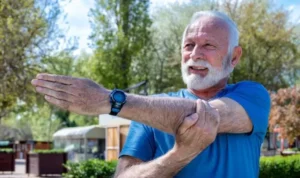 Hombre mayor haciendo estiramiento de brazo aire libre