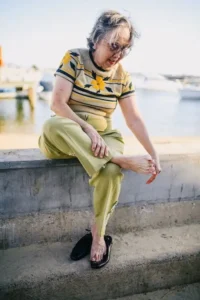 Mujer mayor sentada en muro limpiando los pies