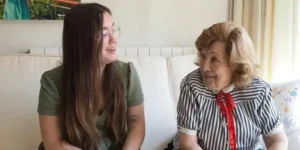 Mujer mayor y joven sonrientes sentadas en sofa de casa