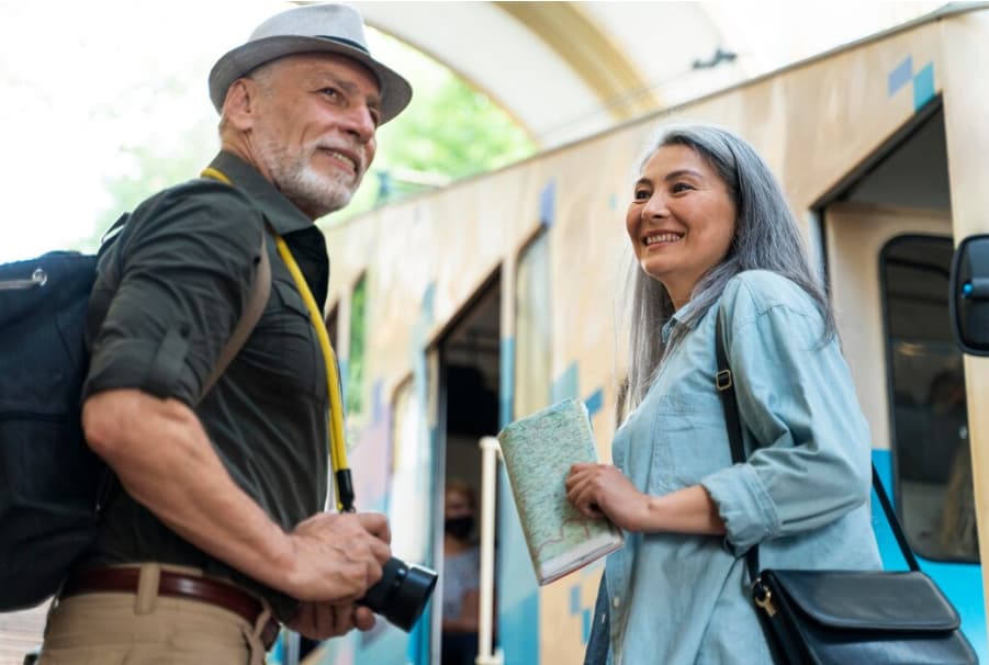 Pareja de personas mayores sonrientes subiendo a un tren