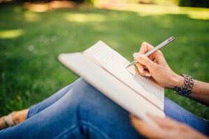 Persona sentada en cesped escribiendo en un cuaderno