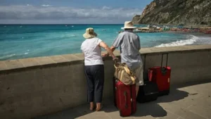 Personas mayores de espalda con maletas en un mirador de la playa