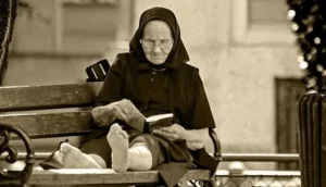 Mujer mayor con pañuelo negro en la cabeza leyendo un libro en un banco