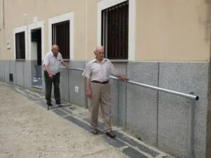 Personas mayores andando por la calle accesible con barras de apoyo en fachadas pescueza