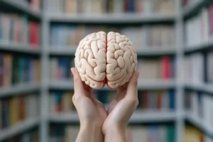 Cerebro cogido entre las manos con una biblioteca al fondo