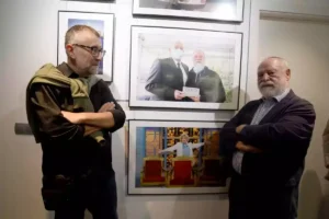 Dos hombres mayores al lado de un cuadro colgado en la pared de una exposición