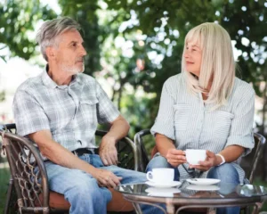 Hombre y mujer mayores sentados en jardín conversando y tomando un café
