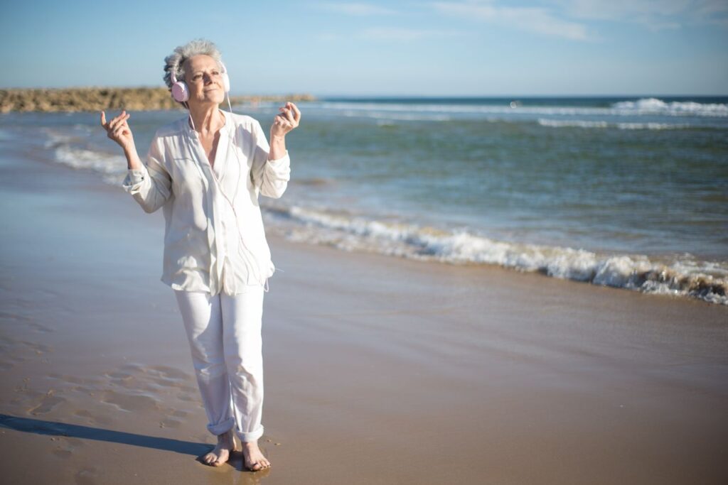 Senior woman with headphones enjoying music on a sunny beach in Portugal.