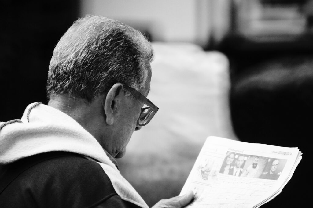 A senior man absorbed in reading a newspaper, captured in a classic monochrome style.