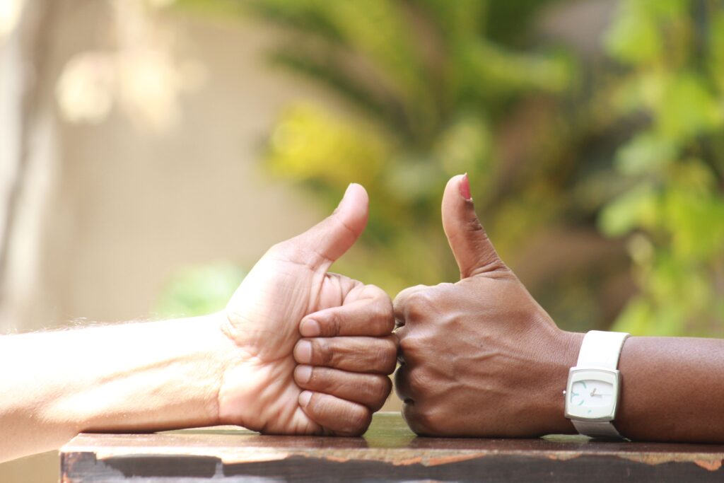 Close-up of two people giving thumbs up outdoors, symbolizing agreement.