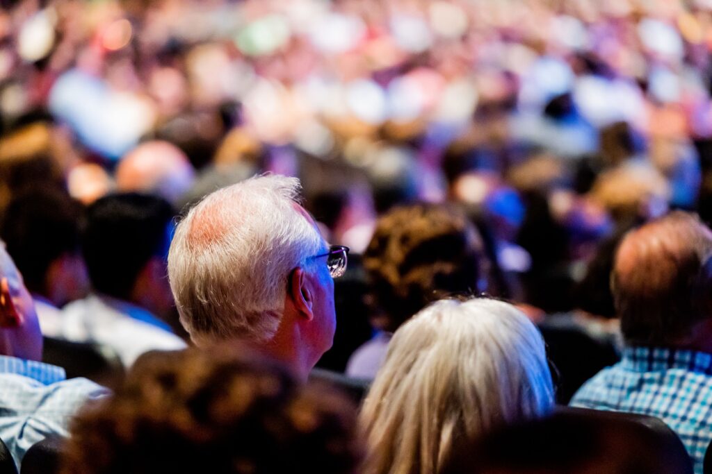 A vibrant crowd of adults attending a conference, viewed from behind.