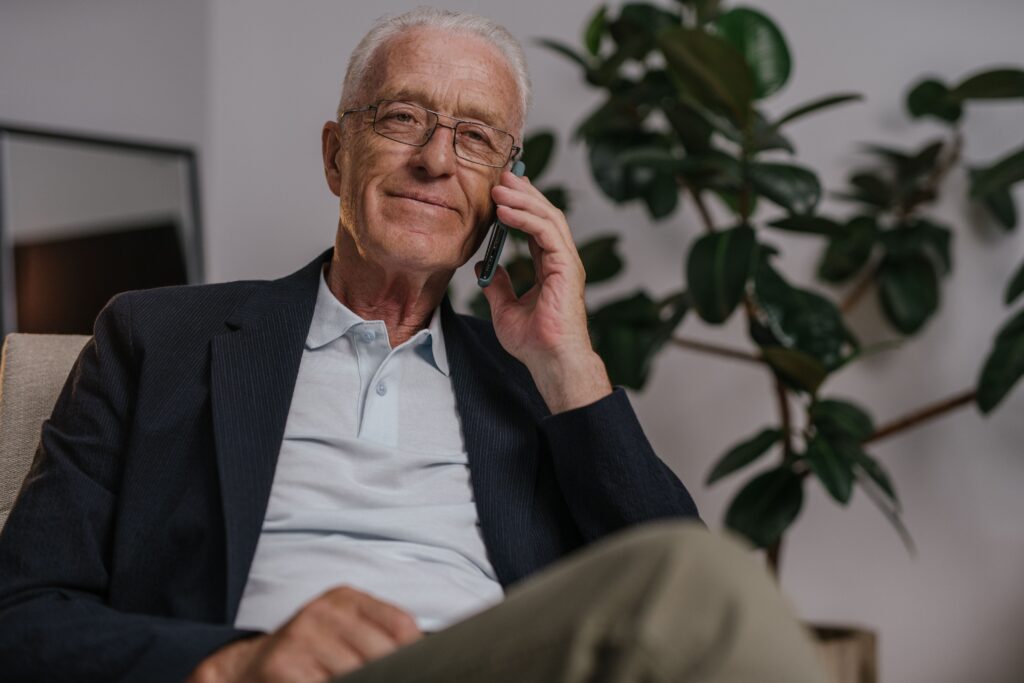 Elderly man with glasses making a phone call indoors, showing relaxed mood.