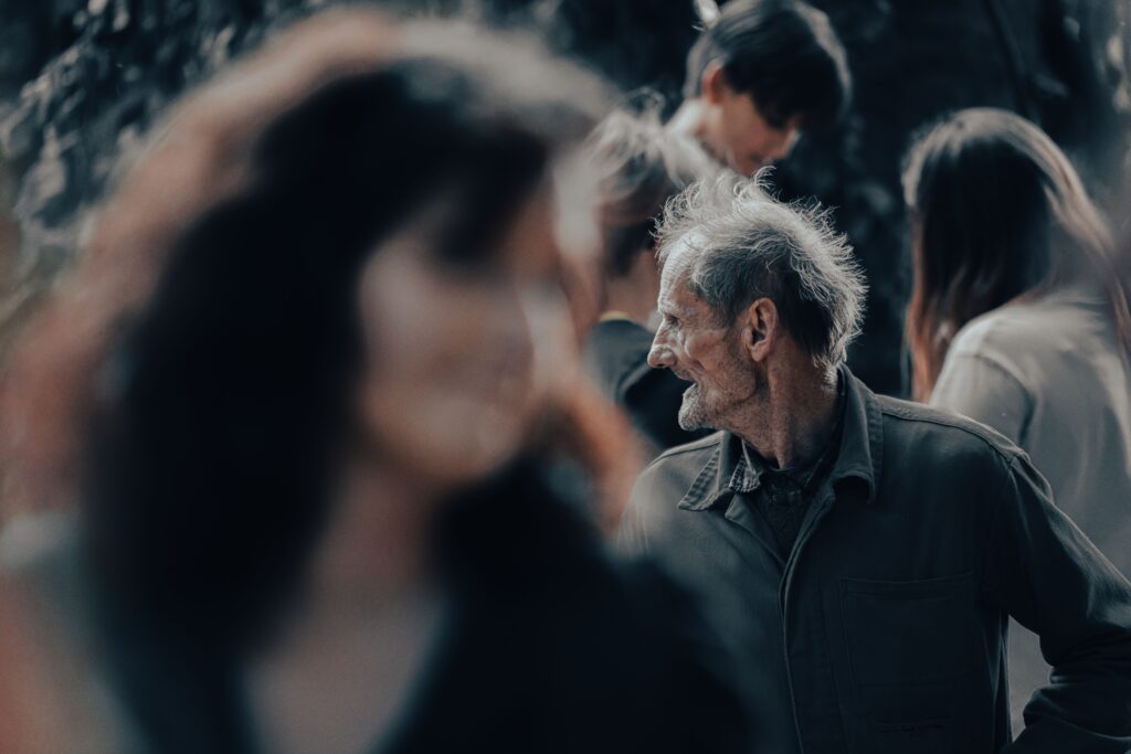 A senior man with a gentle smile stands among blurred people in Prague.