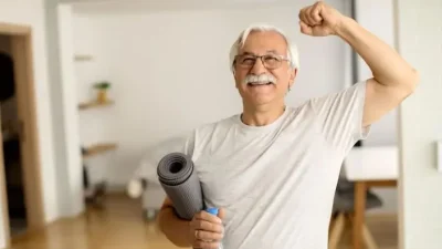 Hombre mayor sonriente sosteniendo esterilla y levantando un brazo