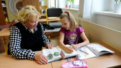 Mujer mayor enseñando libro en colegio a niña